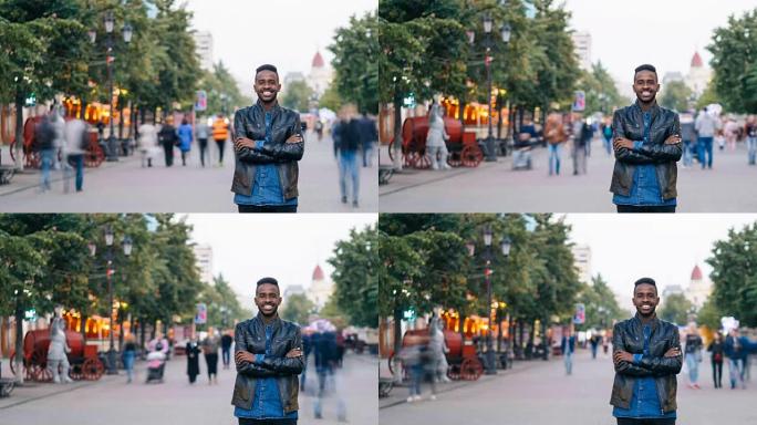 微笑的非洲裔美国男子独自站在市中心，双手交叉，享受城市生活，看着相机。青年和生活方式概念。