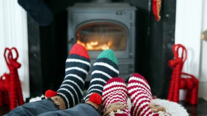 穿着圣诞袜的高级夫妇在燃木炉上暖脚的特写