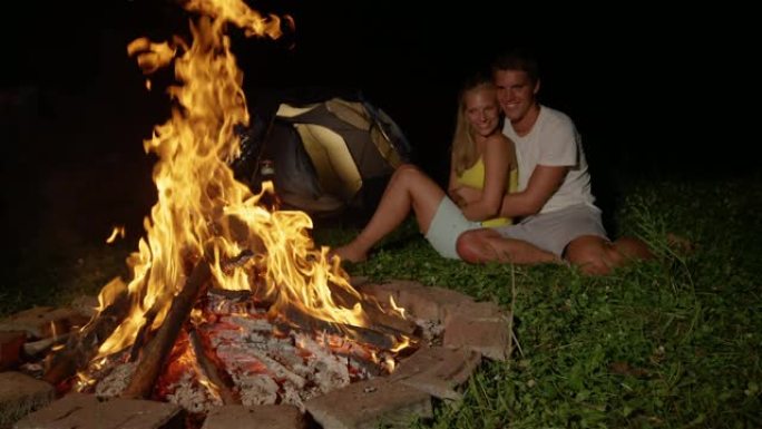 特写: 开朗的高加索夫妇坐在温暖的篝火旁拥抱。