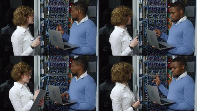 黑色IT专家在服务器机柜中与女同事交谈