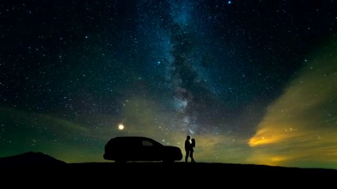 男人和女人站在一辆汽车旁，面对星空。时间流逝