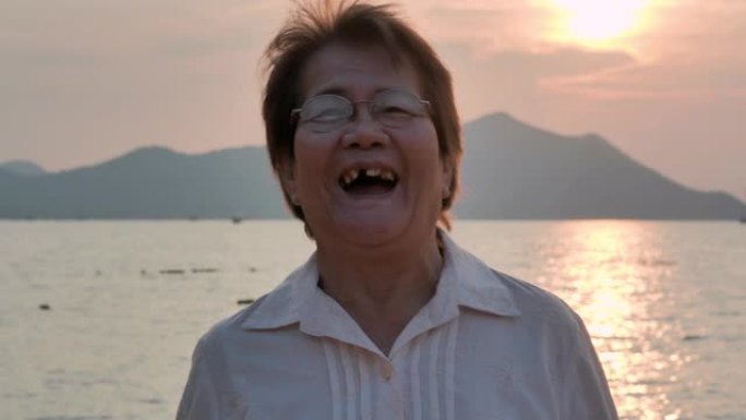 日落时在美丽的大海前笑的亚洲高级女性肖像。人，假期，健康，生活方式，退休，肖像，旅行。高级肖像
