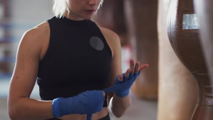 女拳击手在健身房训练，将包裹放在站在出气筒旁边的手上