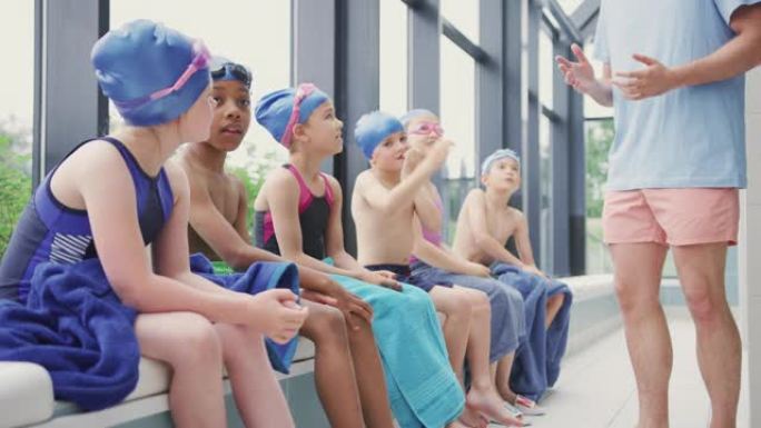 男教练为孩子们提供游泳课简报，因为他们坐在室内游泳池的边缘