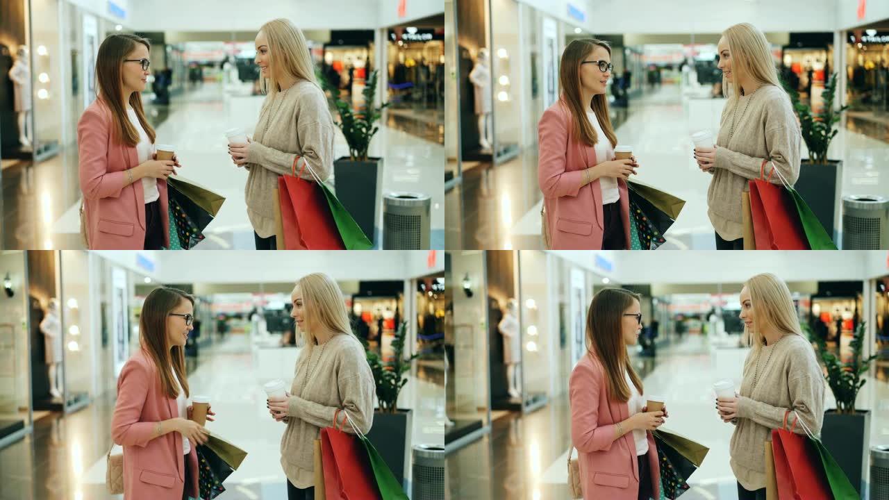 漂亮女孩在商场里聊天，说着笑着拿着纸袋和外卖咖啡。青年生活方式、零售和对话概念。