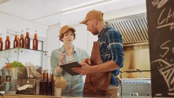 成功的食品卡车男女员工戴着棕色帽子正在使用平板电脑。他们讨论他们的利润和未来的商业计划。出售街头食品