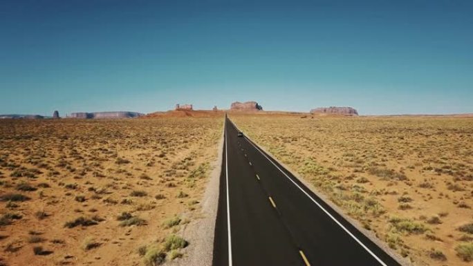 无人机跟随汽车沿着纪念碑谷的标志性美国沙漠公路行驶，并带有大悬崖山脉的天际线。