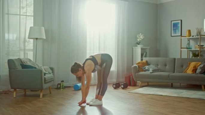 穿着运动上衣的美丽匀称的健身女孩正在她明亮宽敞的起居室里做伸展瑜伽练习，室内装饰现代。