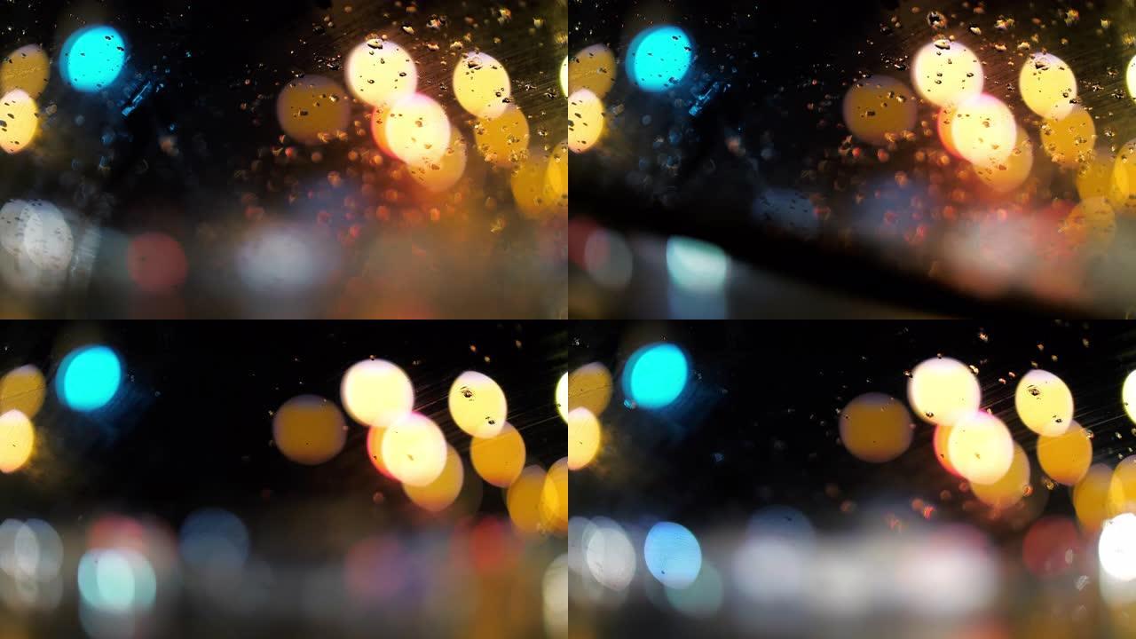 带有模糊的bokeh圆圈交通信号灯背景的汽车上的雨滴