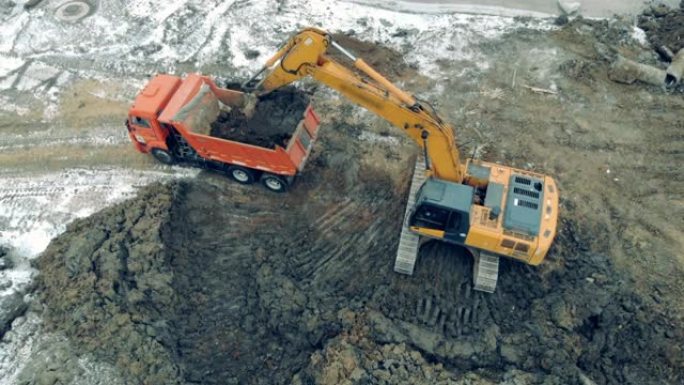 挖掘机和卡车工作的建筑工地上方的鸟瞰图。装载机将石头和沙子放入卡车。
