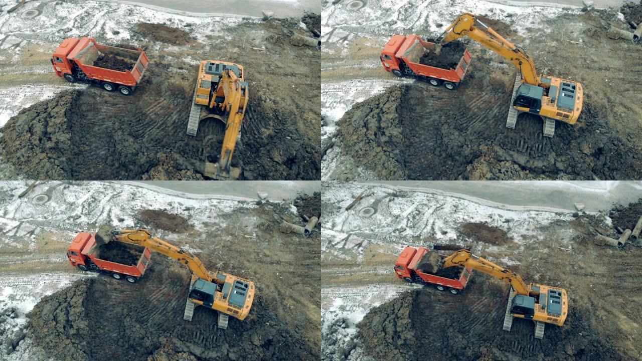 挖掘机和卡车工作的建筑工地上方的鸟瞰图。装载机将石头和沙子放入卡车。