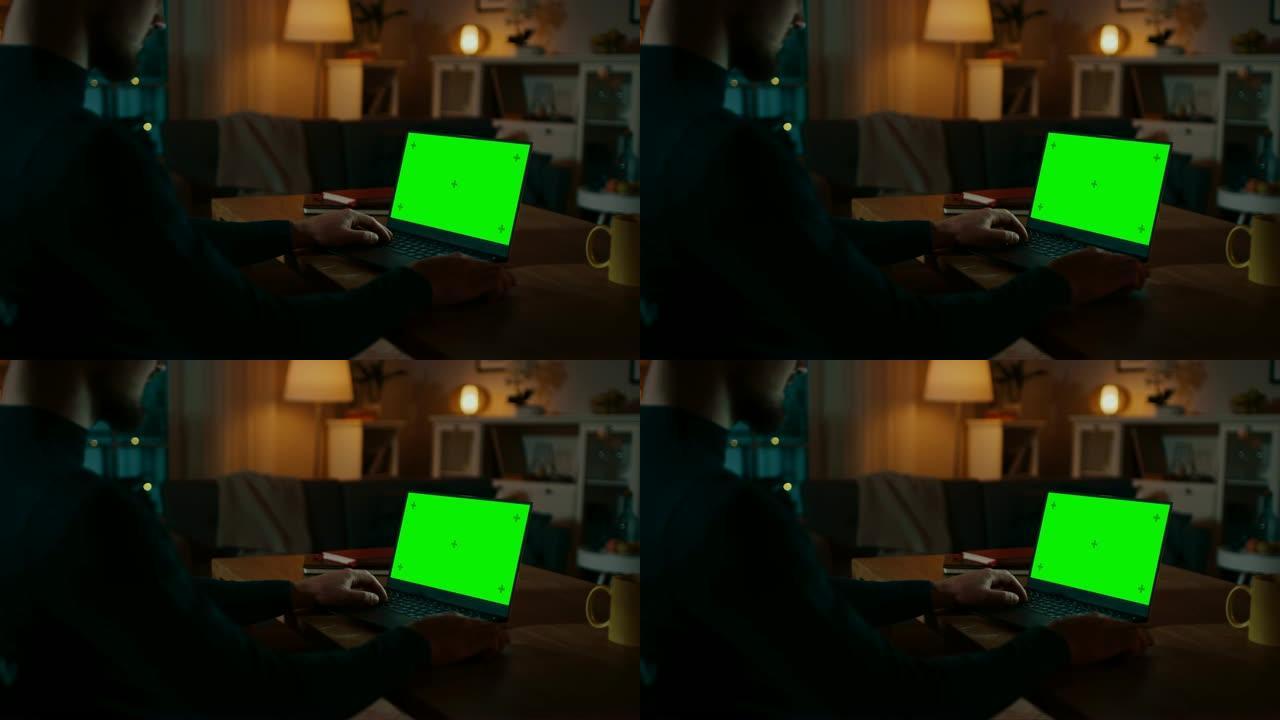肩膀上的镜头: 坐在办公桌前的男人在带有绿色色度键屏幕的笔记本电脑上工作。深夜在她的客厅里，男人使用