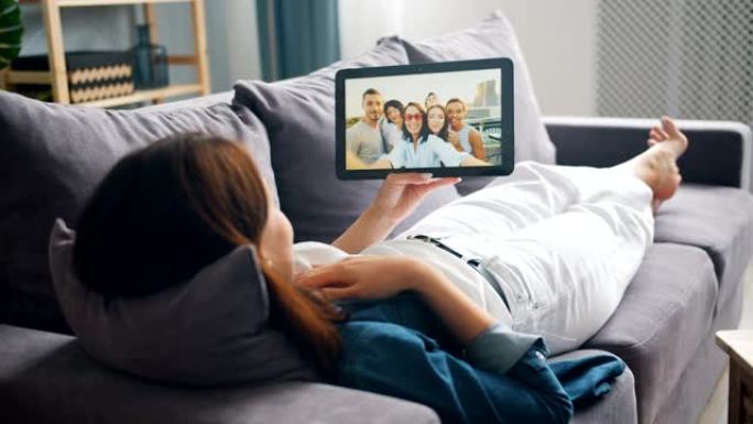 年轻女子用平板电脑与躺在沙发上的朋友聊天进行视频通话