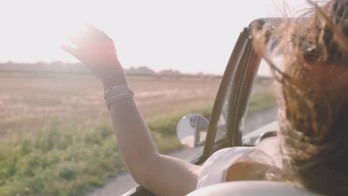 SLO MO无忧无虑的年轻女子沿着阳光明媚的乡村田野驾驶敞篷车