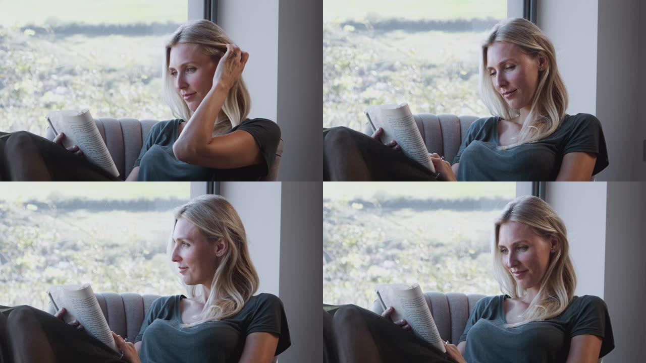 女人在家靠窗的椅子上放松阅读书籍