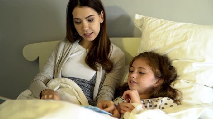 妈妈躺在床上为女儿读睡前故事。单身母亲定期给女儿读故事。带着爱，希望你的孩子快乐
