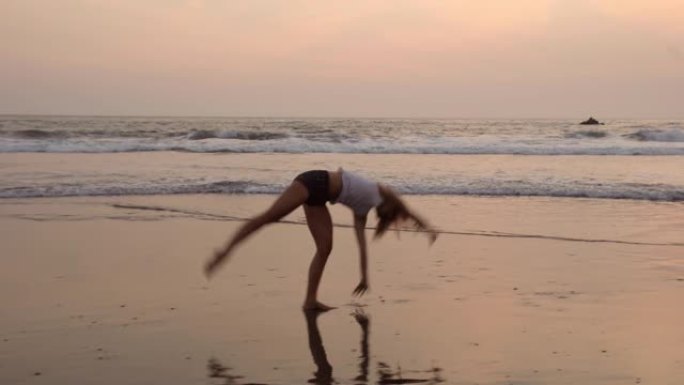 日落时在海洋海滩上做侧翻的年轻运动女人