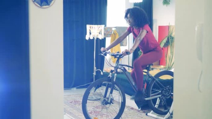 非洲妇女正在家里骑自行车练习。在家运动，在家健身的概念。