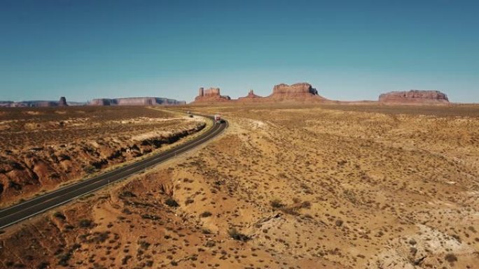 在美国纪念碑谷，红色货运卡车沿着沙漠公路行驶，具有惊人的山天际线的空中拍摄。