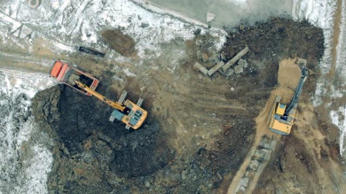在采石场用沙子和石头工作的工业拖拉机。挖掘机和卡车工作的建筑工地上方的鸟瞰图。