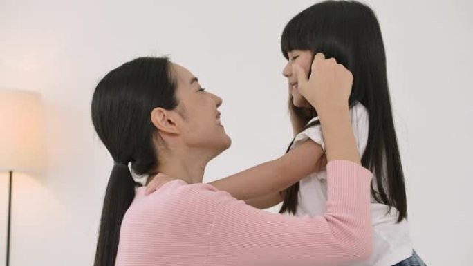 年轻的亚洲母亲在家卧室亲吻她的小女儿。