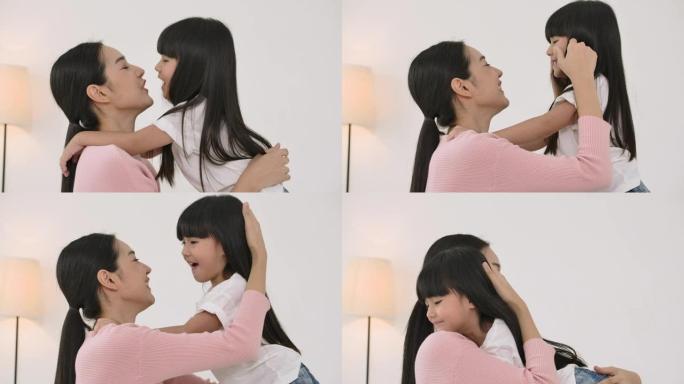 年轻的亚洲母亲在家卧室亲吻她的小女儿。
