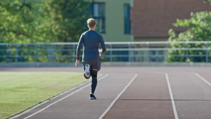 穿着灰色衬衫和短裤的微笑运动健美男子在体育场慢跑。在一个温暖的夏日下午，他跑得很快。运动员做他的常规