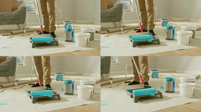 一个男人在长柄滚筒上涂上浅蓝色油漆的特写镜头。油漆在托盘里。家里的房间装修。