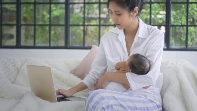 母亲使用笔记本电脑并将男婴抱在怀里，慢动作
