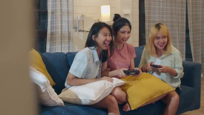 一群亚洲女性夫妇在家玩游戏，女性使用操纵杆在夜晚的客厅沙发上一起度过有趣的时刻。青少年青年朋友足球迷