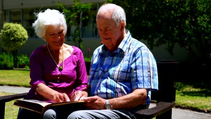 活跃的高加索高级夫妇在养老院4k花园里看相册的前视图