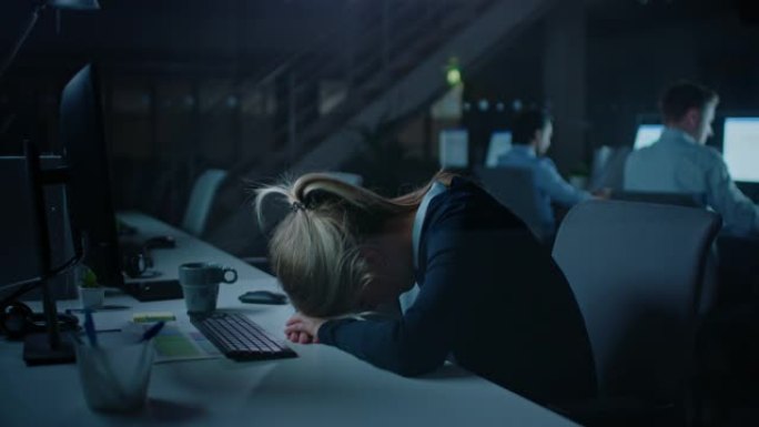 晚上在办公室过度劳累的女上班族绝望地使用台式电脑摔倒在手上睡着了。疲惫疲惫的女商人完成重要项目