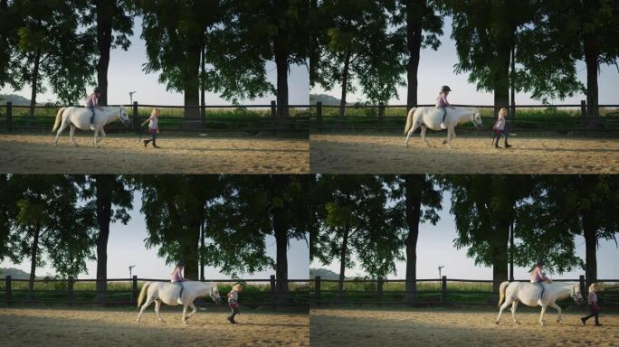 真实的照片是一个小女孩和她的朋友在阳光下骑着一匹白马在马厩里散步