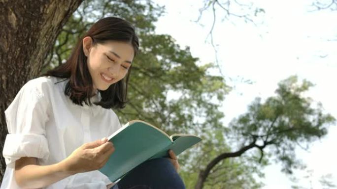 慢动作拍摄年轻迷人的亚洲妇女坐在草地上的夏季公园里，在日落时看书。