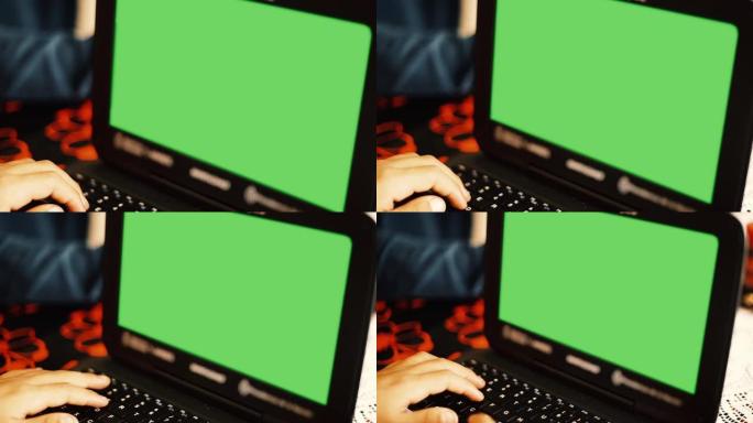 十几岁的男孩在绿色屏幕的黑色笔记本电脑上打字。缩小。