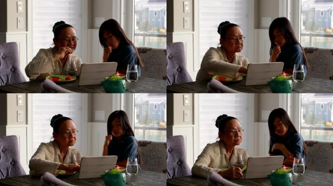 可爱的亚洲孙女和老奶奶在吃4k食物时使用数字平板电脑的前视图
