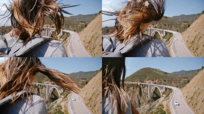 特写后景年轻的旅游女子，头发在强风中飞翔，在大苏尔比克斯比大桥观看令人惊叹的景色。