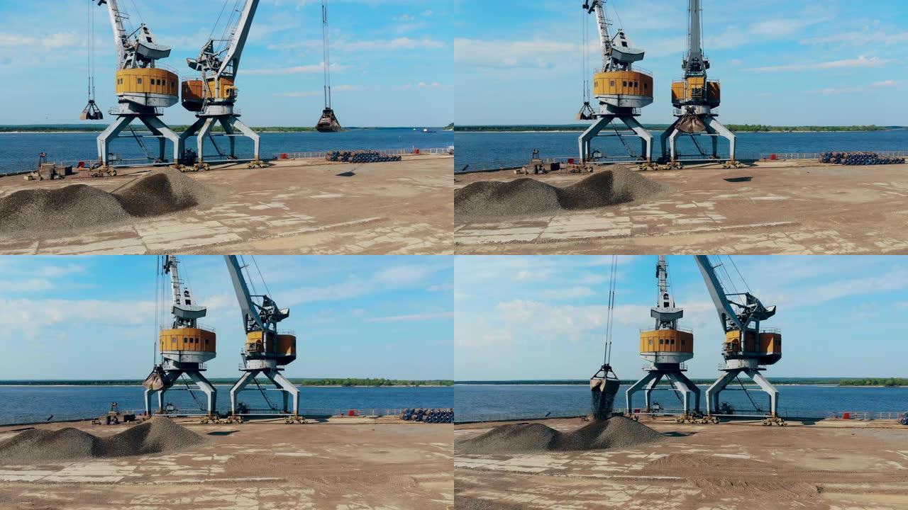 起重机在码头上工作，将碎石放在桶中。