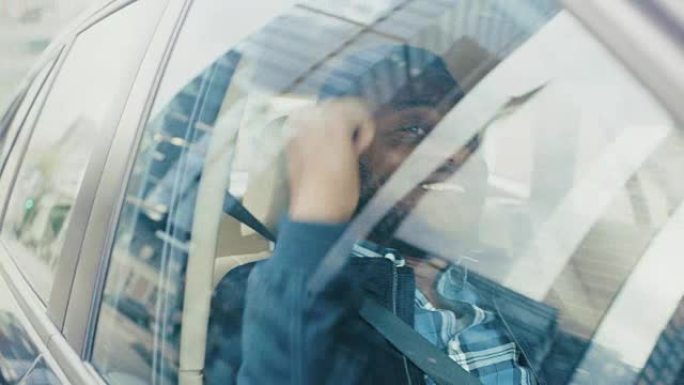 英俊成功的黑人坐在汽车的乘客座位上，他很开心，跳舞。大城市的景色反映在窗口中。摄像机安装在移动汽车外