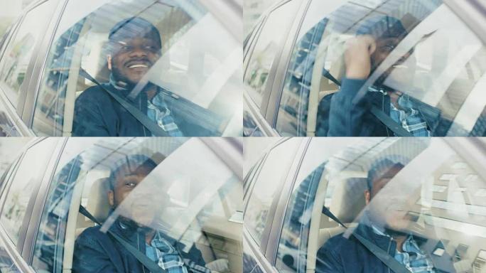 英俊成功的黑人坐在汽车的乘客座位上，他很开心，跳舞。大城市的景色反映在窗口中。摄像机安装在移动汽车外