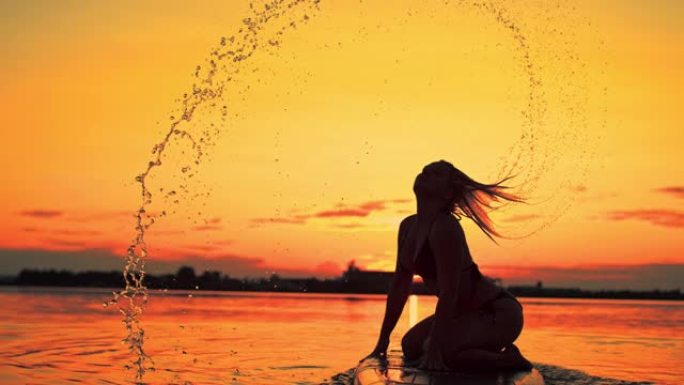 一个女性冲浪者在黄昏时翻转湿头发的超级SLO MO剪影