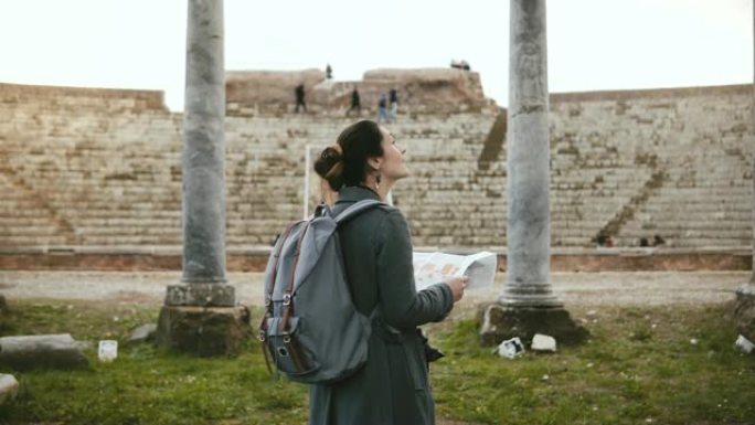 意大利奥斯蒂亚，美丽的旅游女孩背靠背，背包站在古老的圆形剧场柱子前。