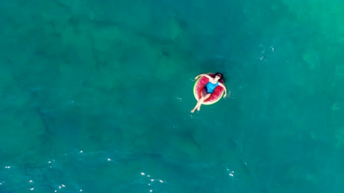 一名妇女在俯视图中漂浮在海中的橡胶圈中