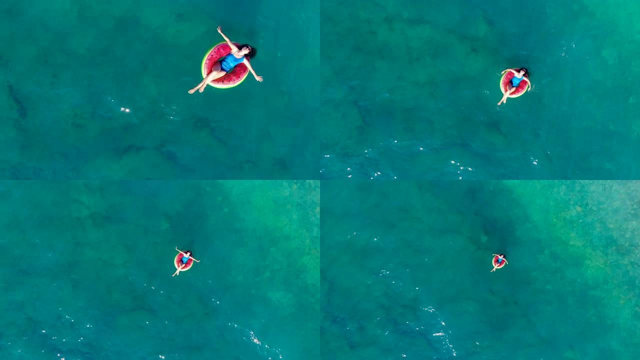 一名妇女在俯视图中漂浮在海中的橡胶圈中