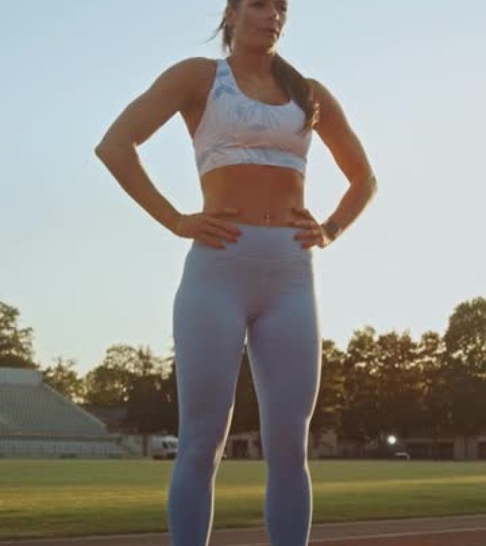 穿着浅蓝色运动上衣和紧身裤的美丽健身女子屏住呼吸，在体育场摆姿势。垂直屏幕方向视频9:16