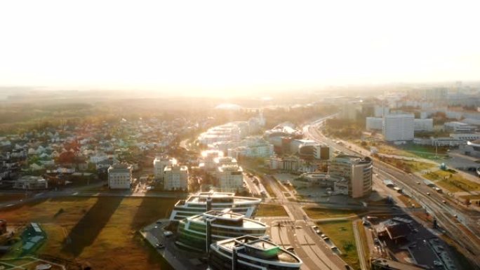 在晴朗的秋日日出时，无人机在白俄罗斯明斯克的现代城市建筑和公园全景上空飞行。
