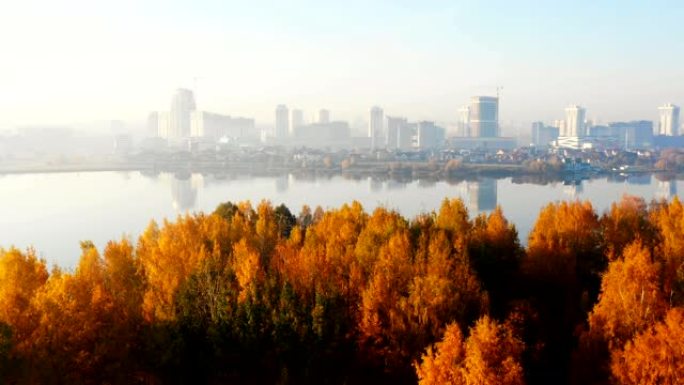 无人机飞向美丽的日出城市建筑，在令人惊叹的湖水和阳光明媚的黄色秋树上全景。