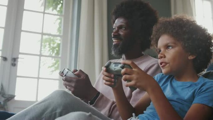 快乐的中年黑人父亲和他十几岁的儿子坐在客厅里的地板上，一起聊天和玩电子游戏，特写