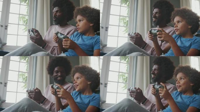 快乐的中年黑人父亲和他十几岁的儿子坐在客厅里的地板上，一起聊天和玩电子游戏，特写