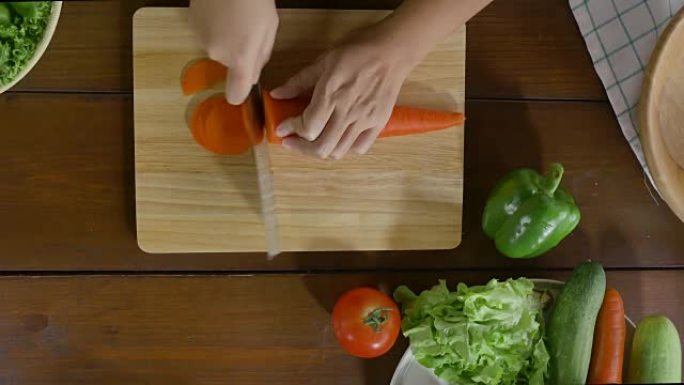 女酋长制作沙拉健康食品和在厨房切菜板上切碎胡萝卜的俯视图。